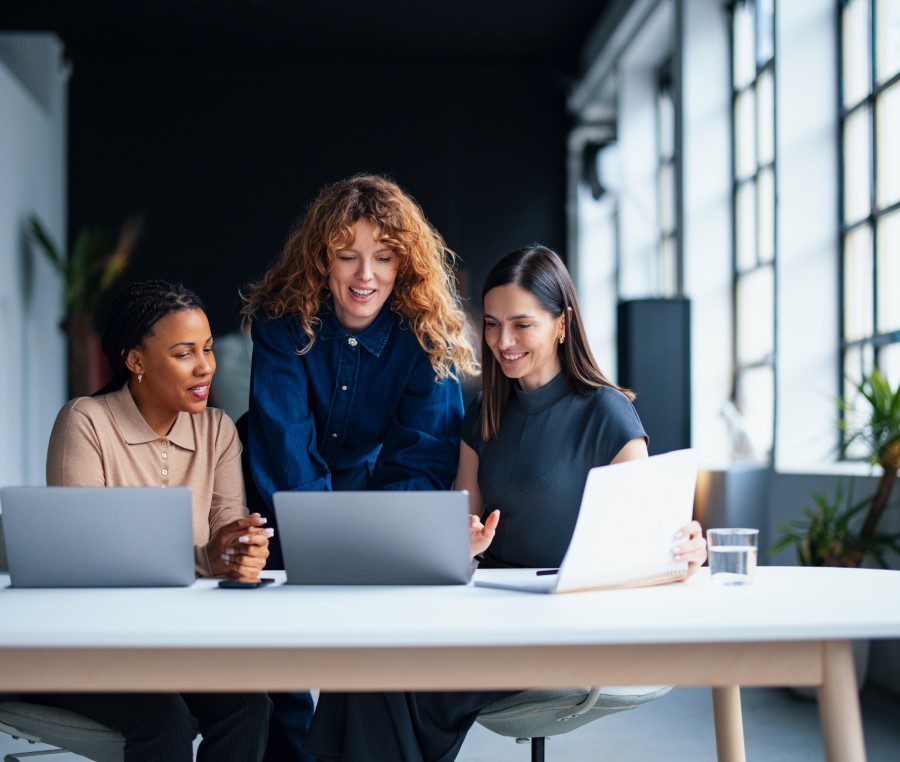 Three women collaborating at work with laptops.