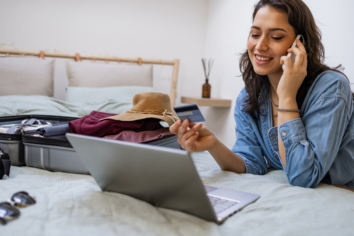 Happy woman talking won the phone phone and using laptop to make flight reservation
